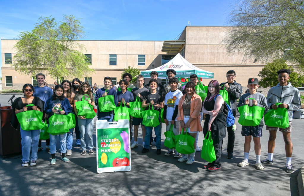 A large group of students stand smiling with their Yolo Food Bank totes full of food.