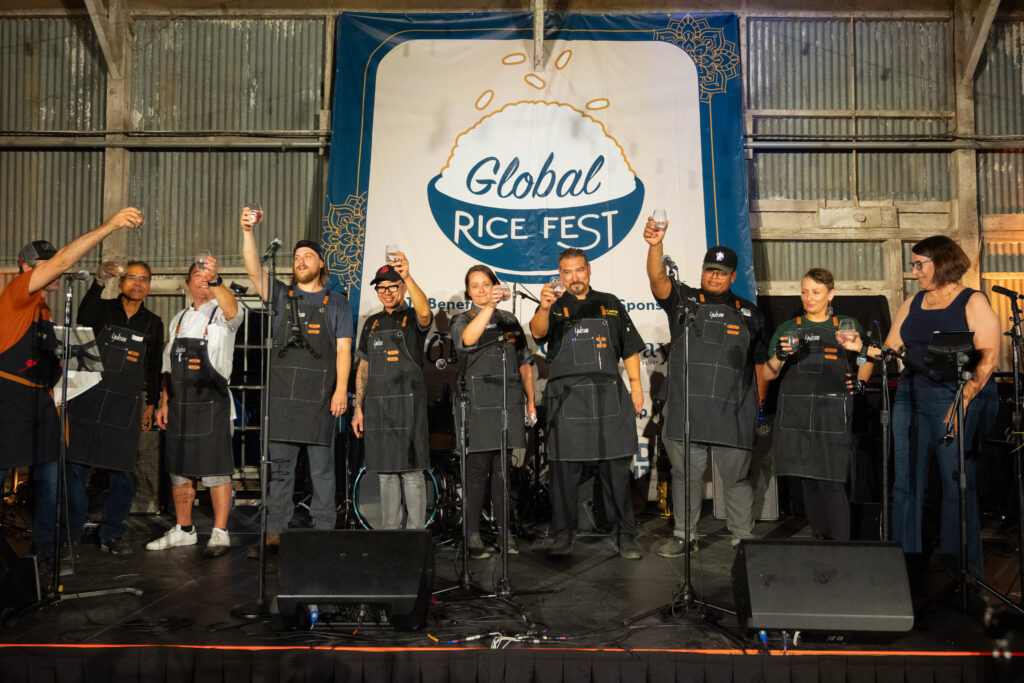 Line of chefs and Karen Baker hold glasses in the air on stage to toast the event